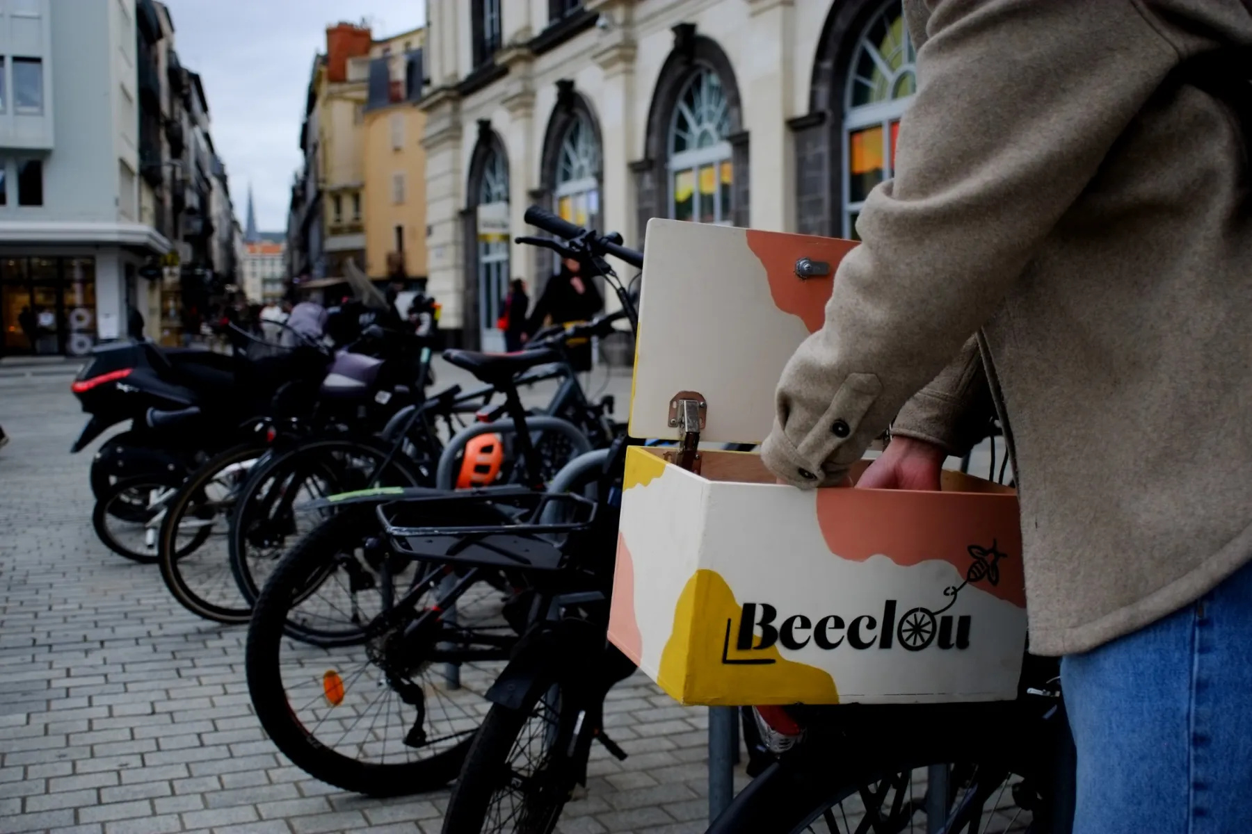 Un cycliste ouvre la boîte Beeclou fixée sur son porte-bagages, dans une rue piétonne.