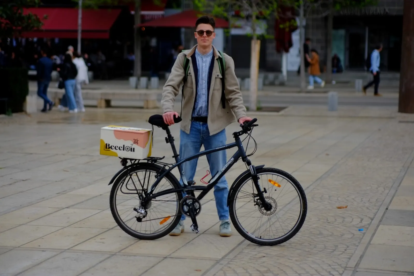 Un cycliste debout à côté de son vélo, une boîte Beeclou sur le porte-bagages.