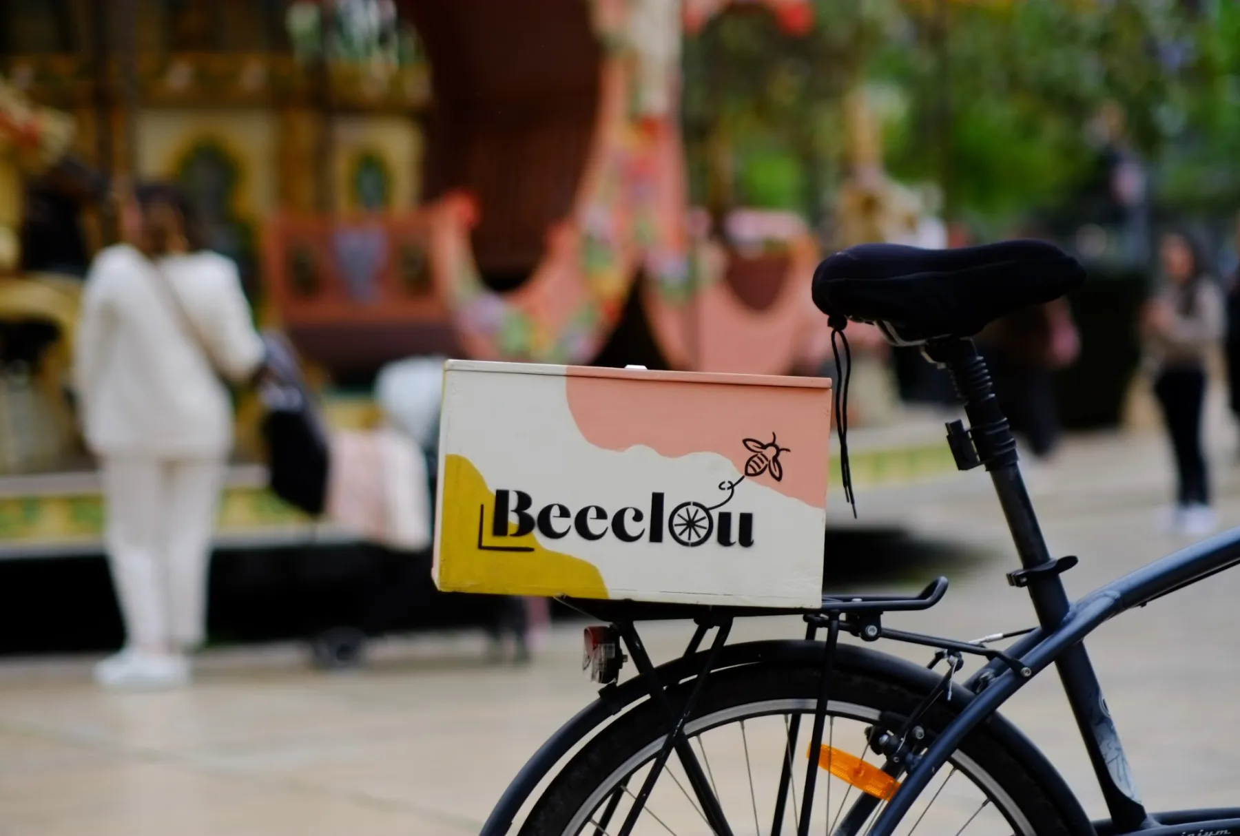 Un vélo équipé de la boîte Beeclou devant un manège, sur une place animée.